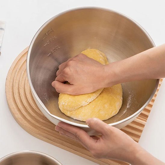 Femme  qui petrit de la pate dans un cul de poule inox